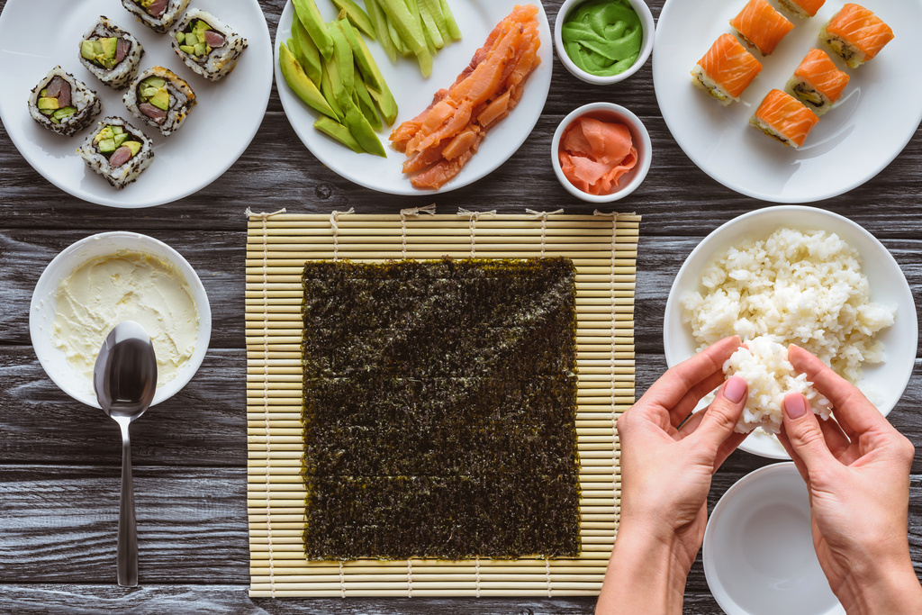 vista superior parcial de la persona que prepara el arroz para el sushi delicioso sobre la mesa de madera
 - Foto, imagen
