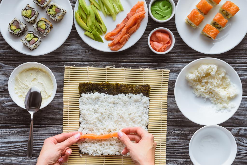 abgeschnittene Aufnahme einer Person, die köstliche Sushi-Rolle mit Lachs, Reis und Nori kocht   - Foto, Bild