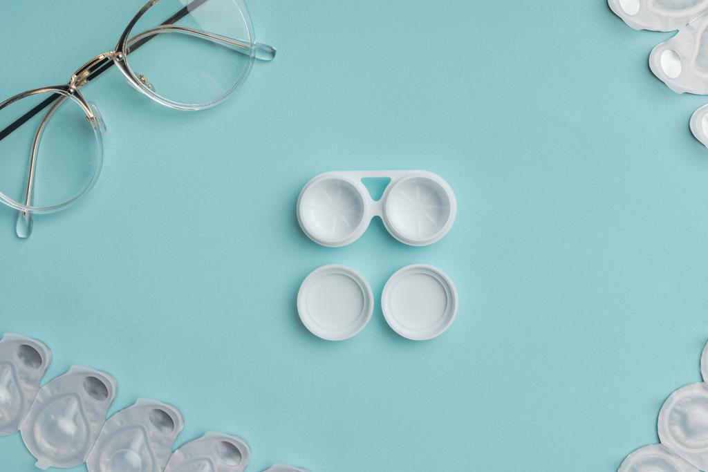 top view of eyeglasses and arranged contact lenses containers on blue background - Photo, Image