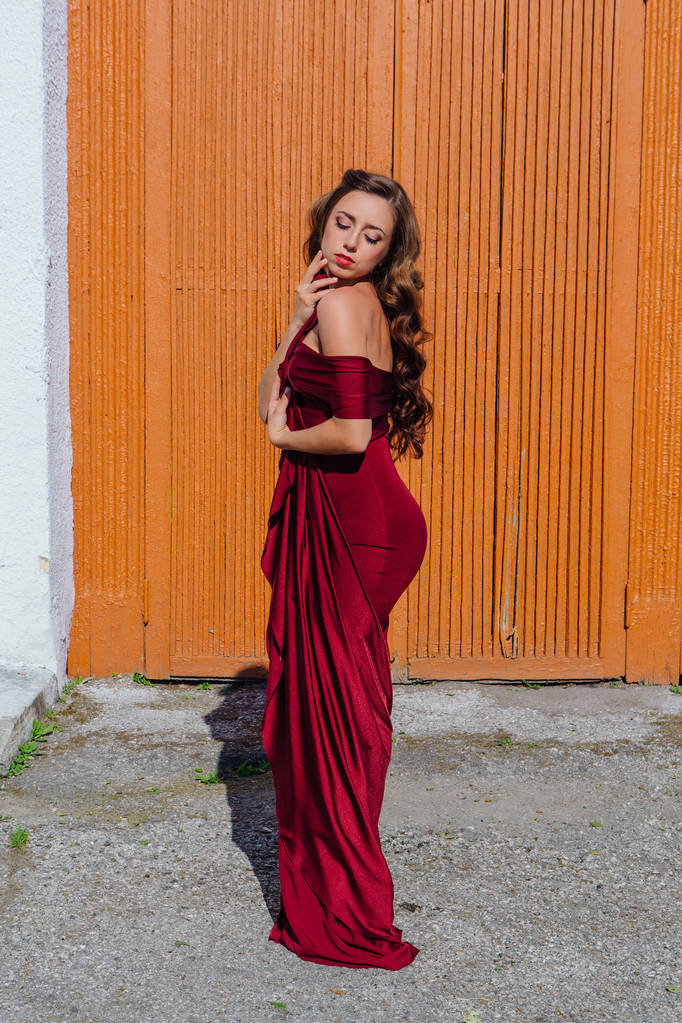 Hermosa joven con un largo vestido de noche rojo con un tren de pie junto a la vieja puerta
 - Foto, imagen