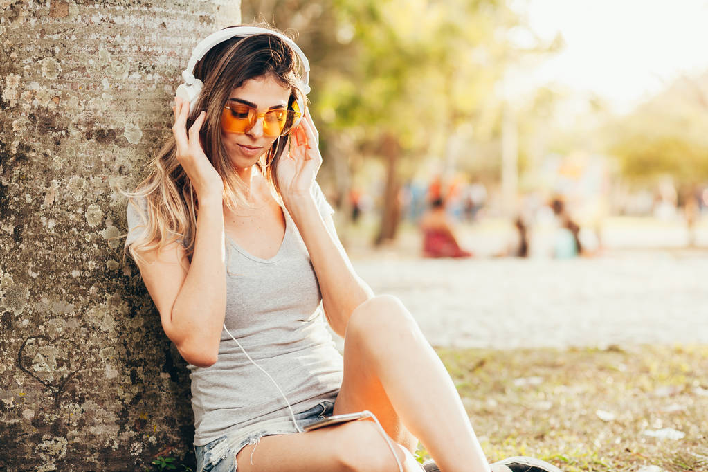 Young woman in the park listening to music on headphones on a sunny day - Photo, Image