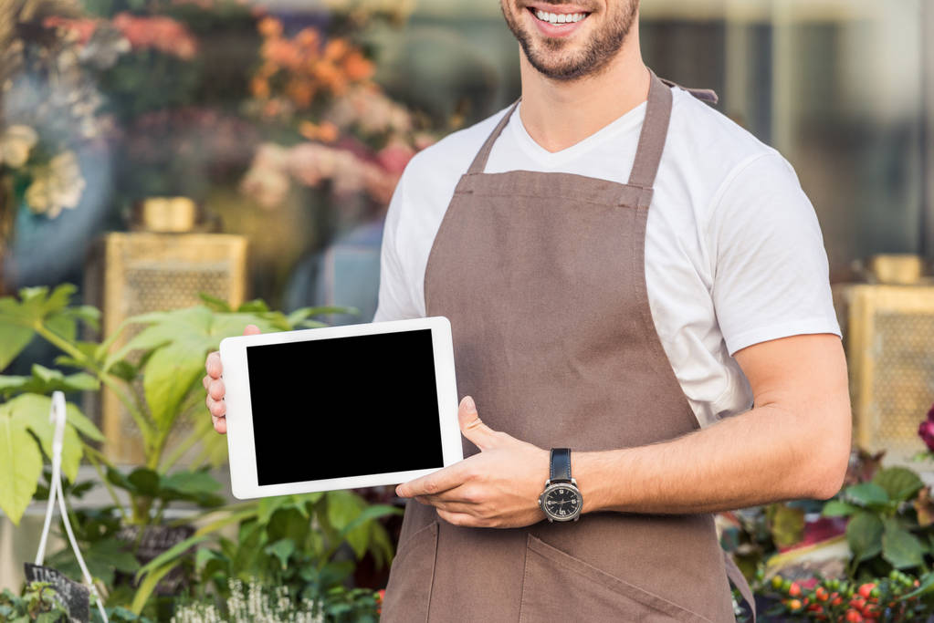 обрезанное изображение улыбающегося флориста, держащего планшет с пустым экраном возле цветочного магазина
 - Фото, изображение