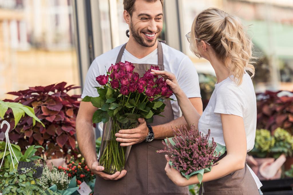 konuşmak ve çiçekçi dükkanı saksılı bitki ve bordo gül ile yakın duran gülümseyen çiçekçi - Fotoğraf, Görsel