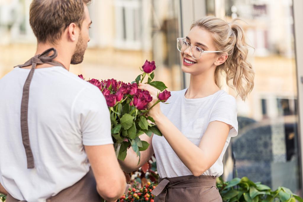 smiling florists selecting burgundy roses near flower shop - Photo, Image
