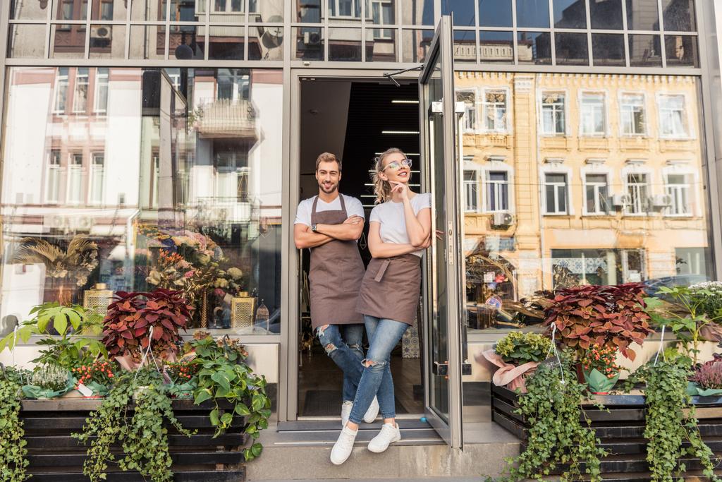 smiling female and male florists standing in open door of flower shop - Photo, Image