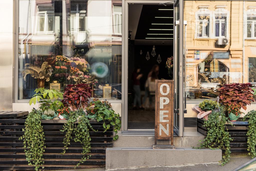 Offenes Schild, Topfpflanzen und spiegelnde Fenster im Blumenladen - Foto, Bild