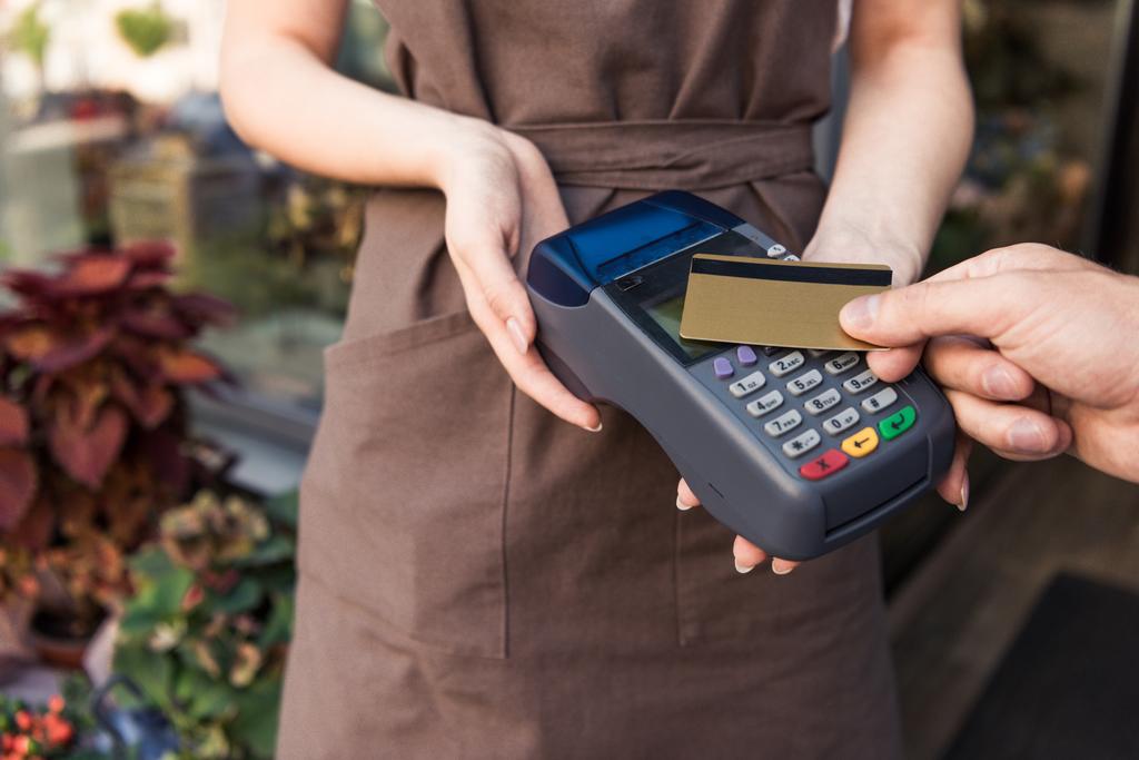 обрезанное изображение клиента, оплачивающего кредитной картой в цветочном магазине, флориста, держащего платежный терминал
 - Фото, изображение