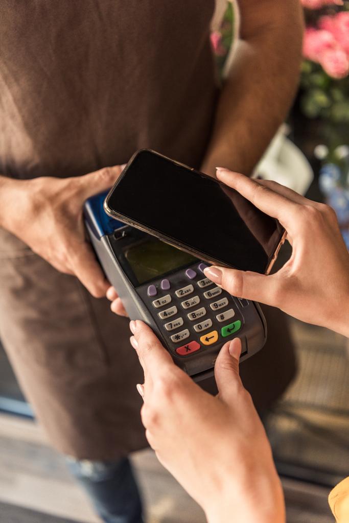 обрезание изображения клиента, делающего бесконтактную оплату со смартфона в цветочном магазине
 - Фото, изображение