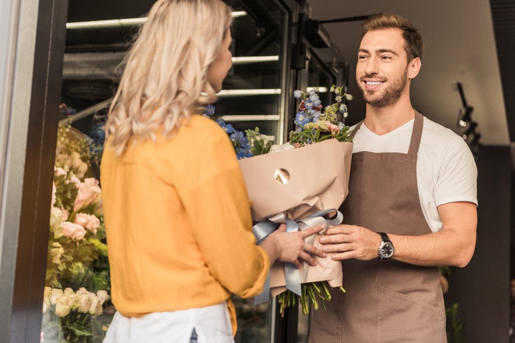 handsome florist giving wrapped bouquet to customer at flower shop - Photo, Image