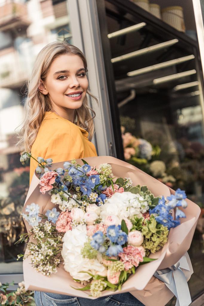 houkutteleva tyttö tilalla kaunis kimppu lähellä kukkakauppa ja katsot kameraa
 - Valokuva, kuva