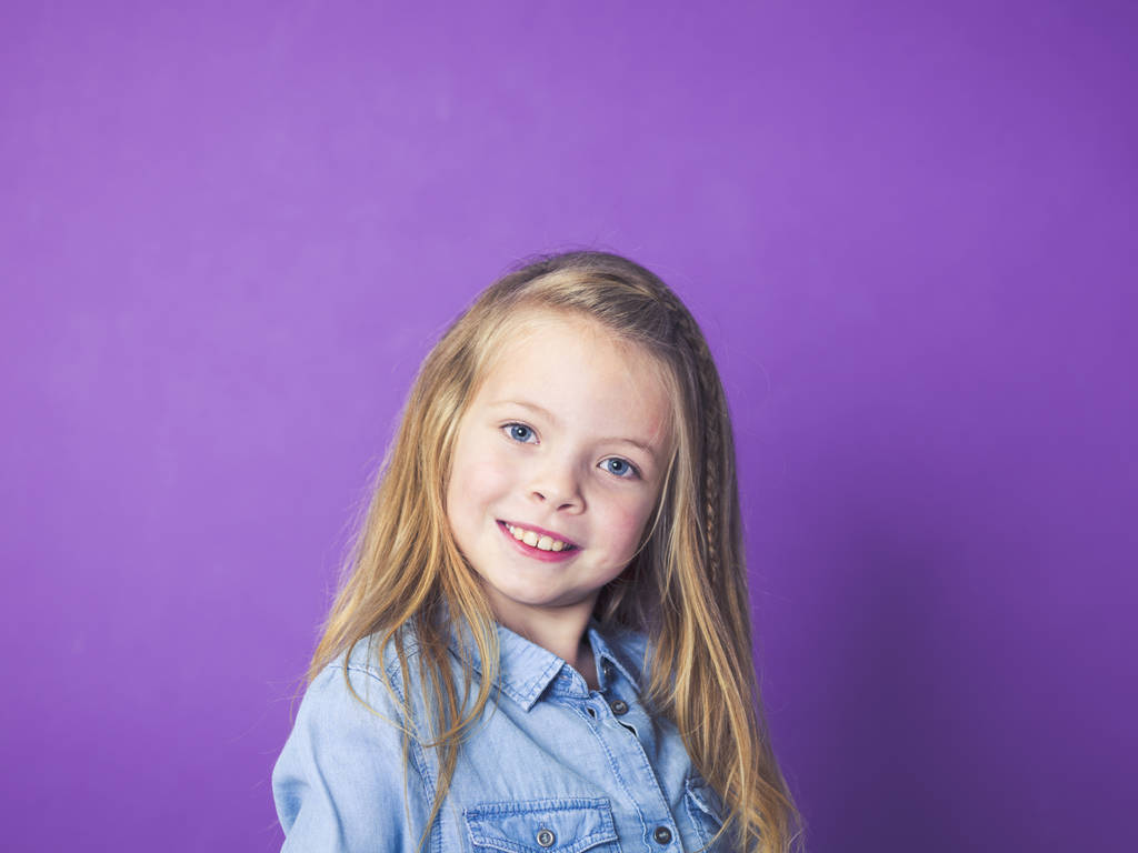 aranyos kis lány visel kék farmer ing lila háttér előtt, a stúdió-portré - Fotó, kép