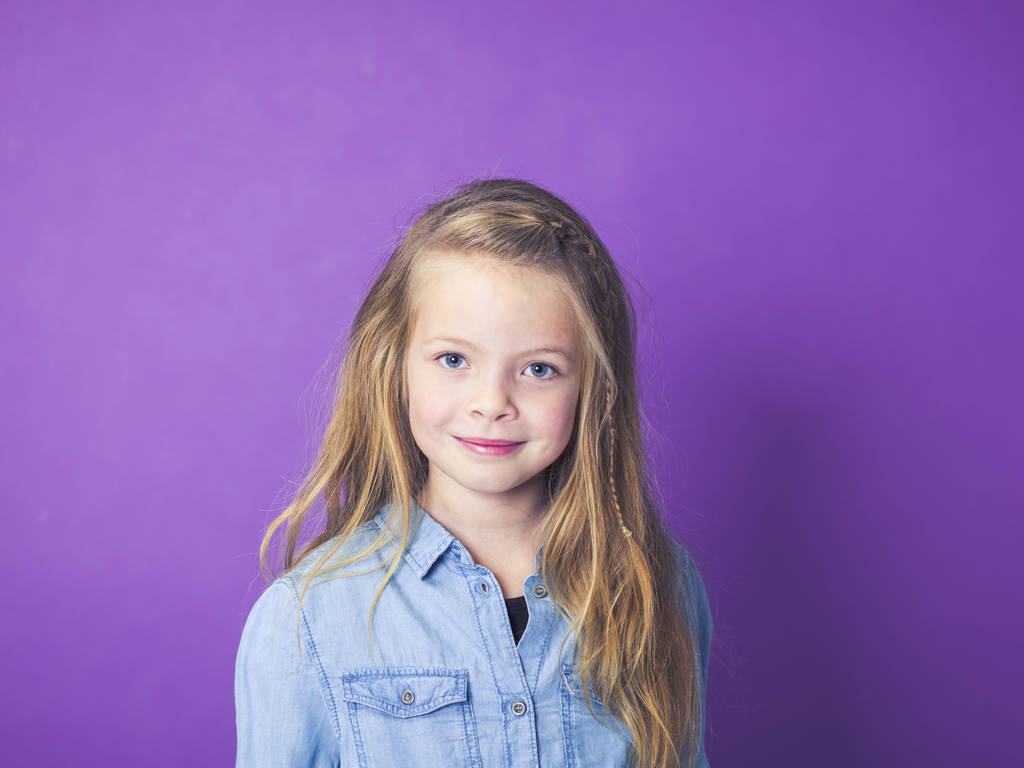 Porträt eines süßen kleinen Mädchens in blauem Jeanshemd vor violettem Hintergrund im Studio - Foto, Bild