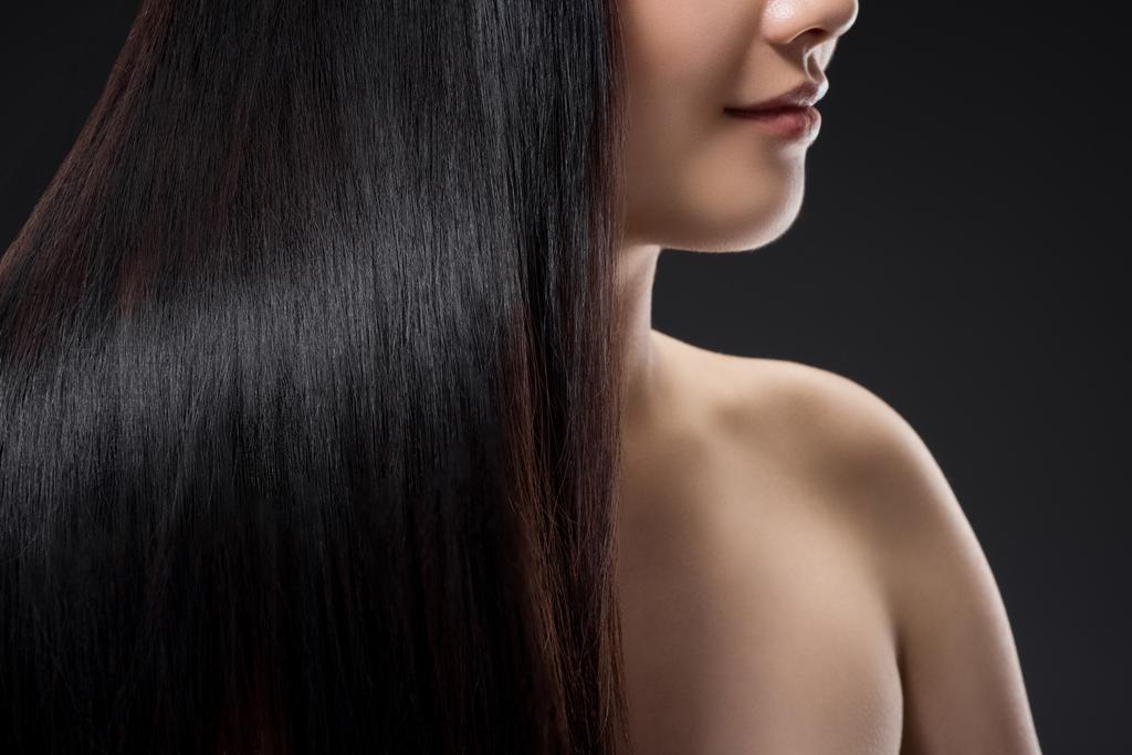 vista parcial de la mujer sonriente con el pelo brillante sano y fuerte aislado en negro
 - Foto, Imagen