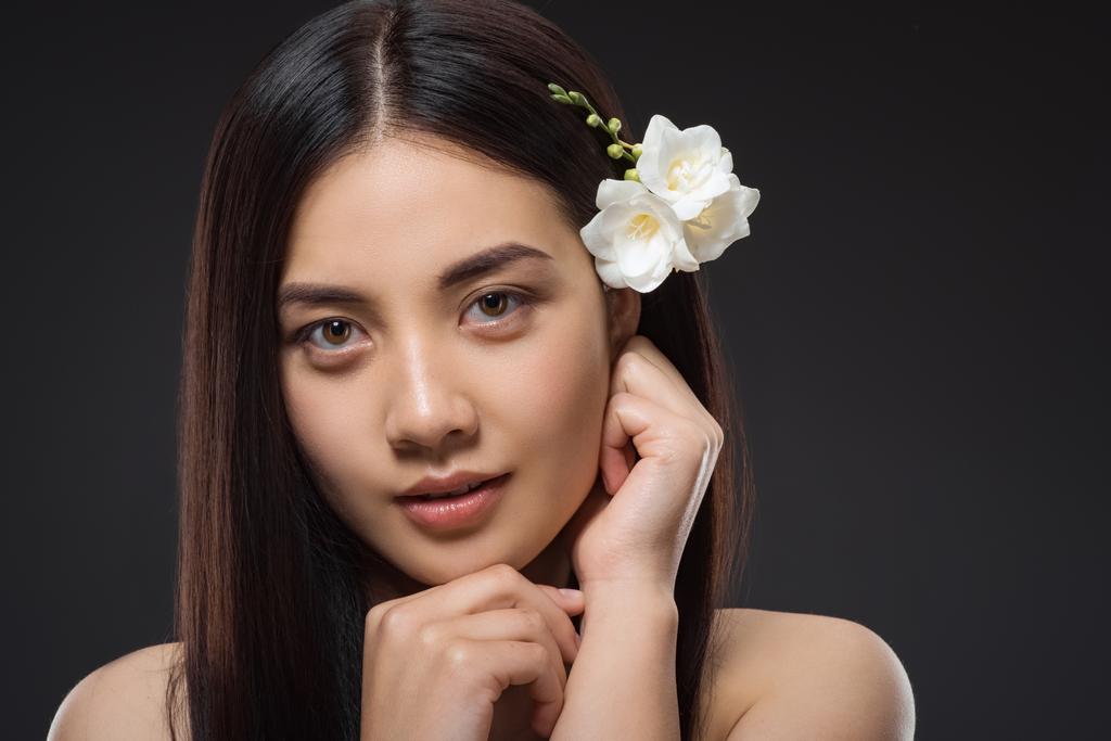 портрет красивой молодой азиатской женщины с белыми цветами в волосах, смотрящей в камеру, изолированную на черном
 - Фото, изображение