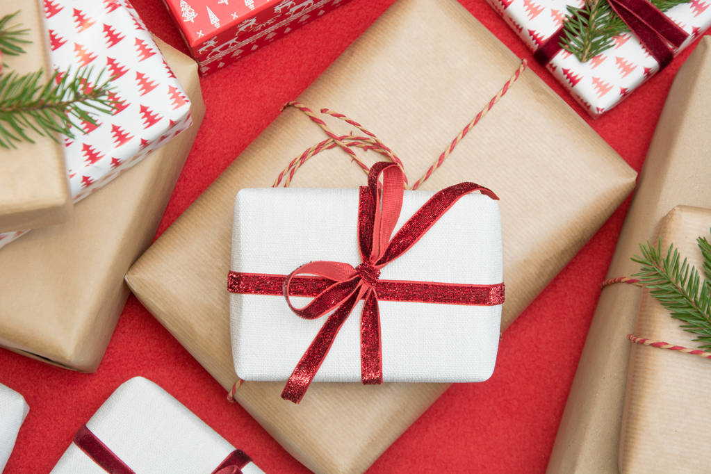 De doos van de gift van Kerstmis verpakt in ornament papier en decoratieve rode koord lint op rode oppervlak. Creatieve hobby, bovenaanzicht. Voorbereidingen treffen voor Xmas. - Foto, afbeelding