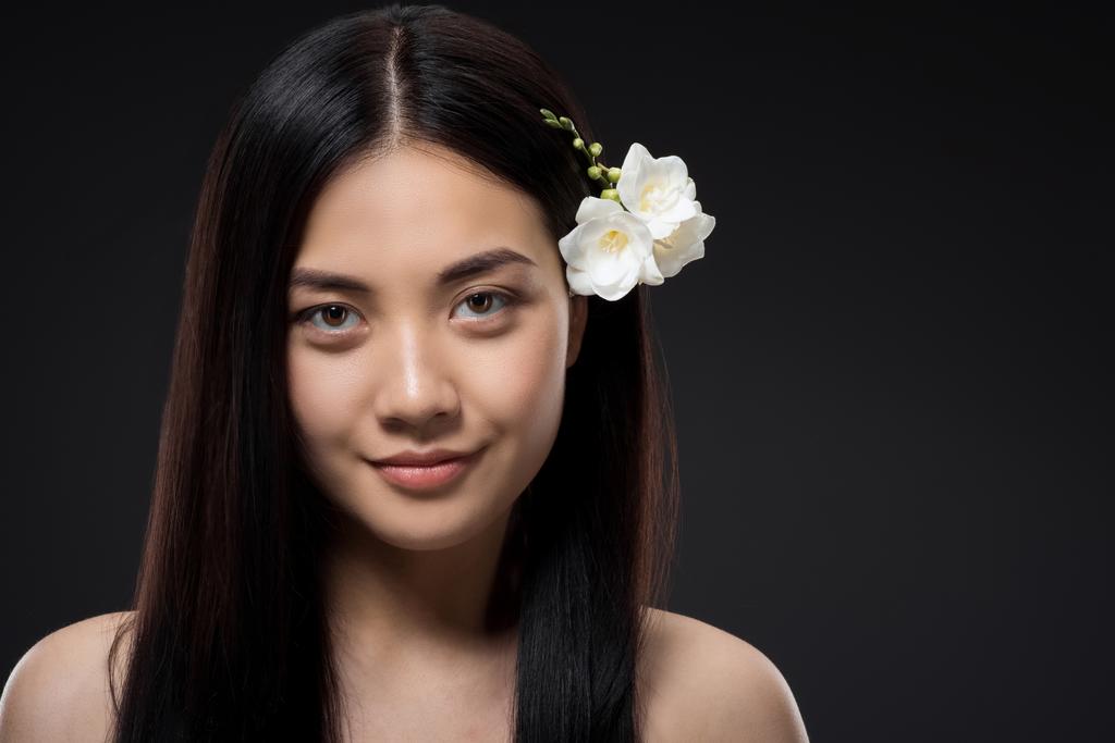 retrato de hermosa sonriente mujer asiática con flores blancas en el pelo aislado en negro
 - Foto, Imagen