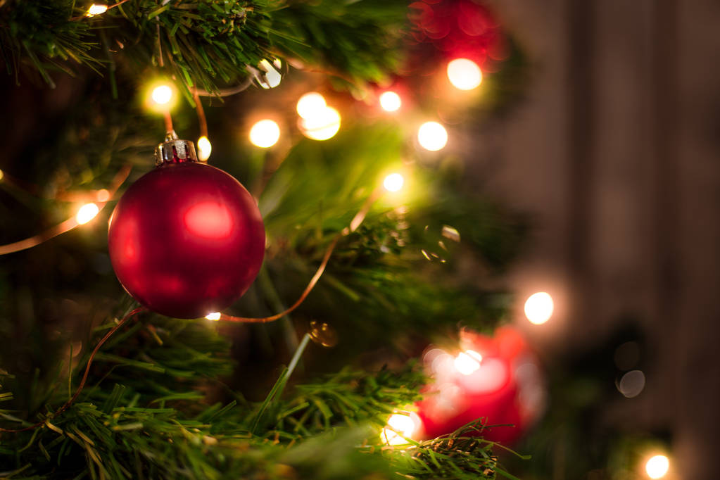 Red Christmas ball on a Christmas tree with a garland on the background of a wooden wall - Photo, Image