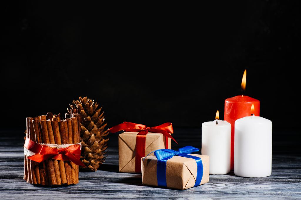 szczegół widokiem płonących świec, sosna stożek i Boże Narodzenie prezenty na drewnianym stole na czarny - Zdjęcie, obraz