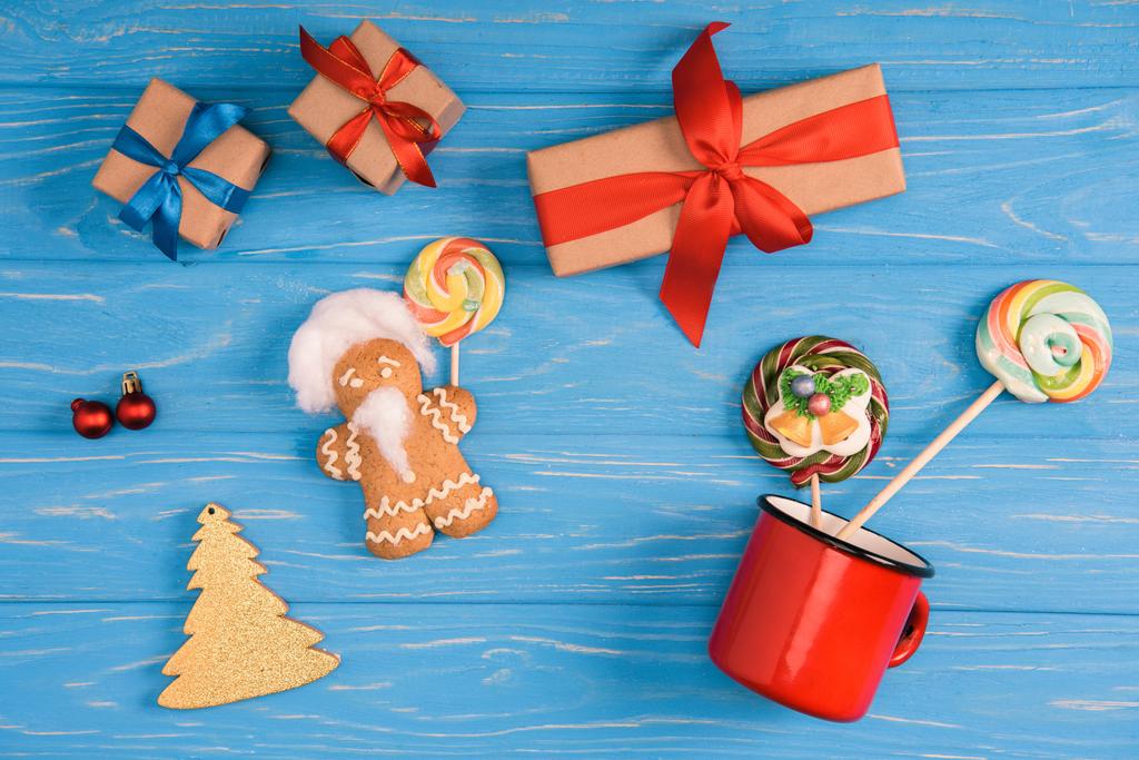 bovenaanzicht van peperkoek cookie, lollies en kerstcadeautjes op blauwe houten oppervlak - Foto, afbeelding