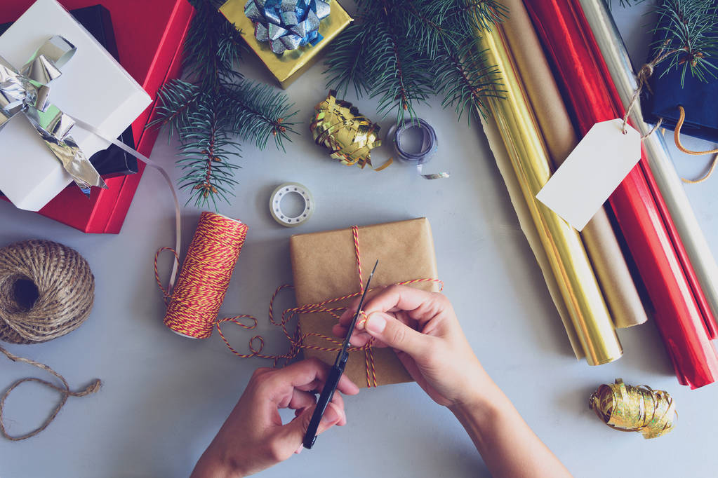 Женские руки украшают подаренную коробку на сером деревянном фоне. Новогодние и рождественские украшения. Toned
 - Фото, изображение