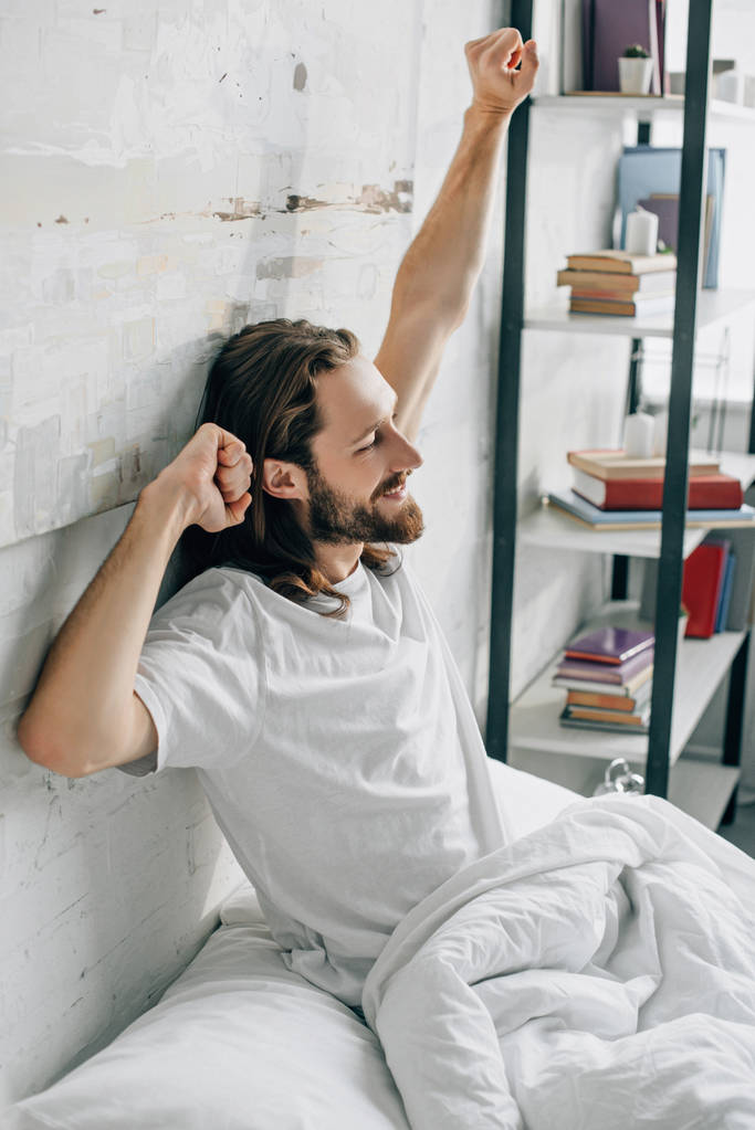 vue latérale du jeune homme barbu aux cheveux longs faisant étirement le matin au lit à la maison
  - Photo, image