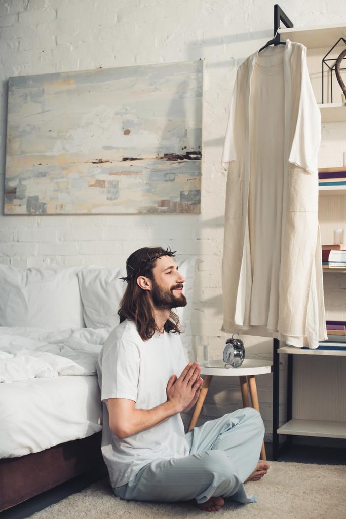 Jesus feliz na coroa de espinhos sentado no chão em posição de lótus durante o tempo da manhã em casa
 - Foto, Imagem
