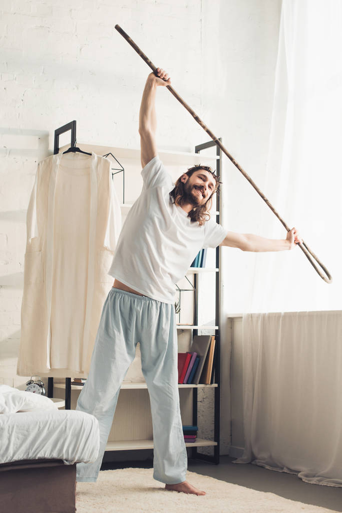 счастливый Иисус в терновом венце делает утреннюю тренировку с деревянным посохом в спальне дома
  - Фото, изображение