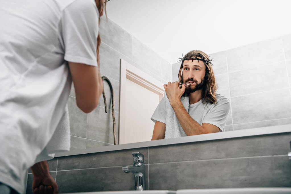 vista parziale di Gesù con asciugamano sopra la spalla lavarsi i denti e guardando il proprio riflesso in bagno
  - Foto, immagini