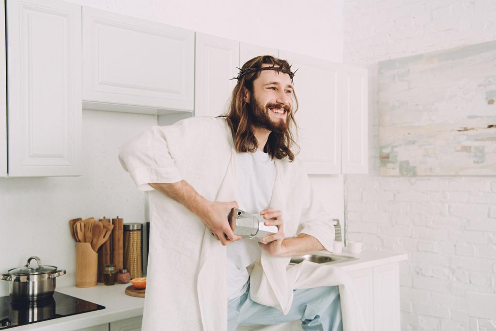 glimlachend Jezus slijpen koffiebonen met handen in handmatige coffeemill in keuken thuis - Foto, afbeelding