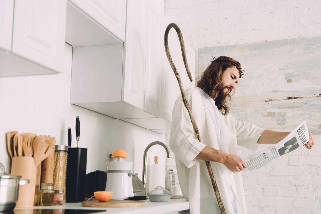 selective focus of Jesus with wooden staff reading business newspaper in kitchen at home - Photo, Image
