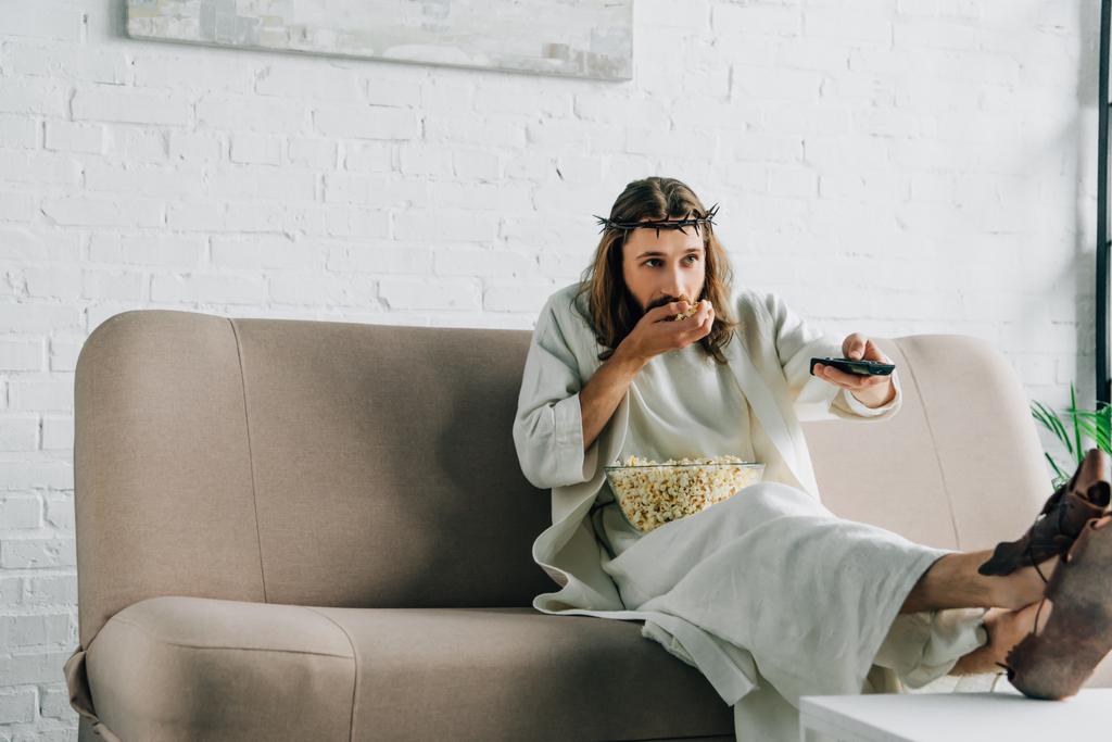 foco seletivo de Jesus na coroa de espinhos assistindo tv e comer pipocas no sofá em casa
 - Foto, Imagem