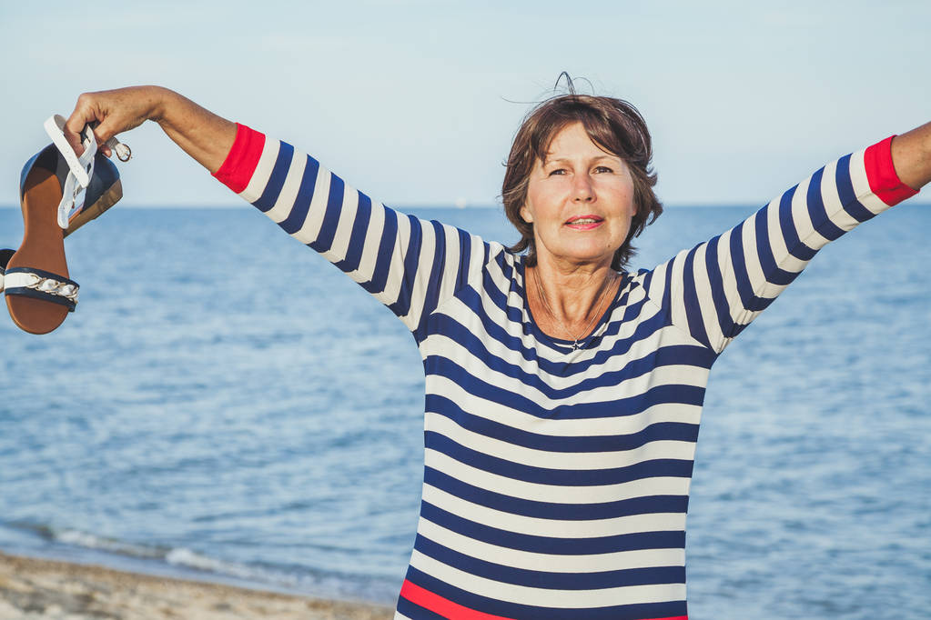 Ηλικιωμένη γυναίκα όμορφη ευτυχώς ύψωσε τα χέρια του στον ήλιο στην παραλία - Φωτογραφία, εικόνα