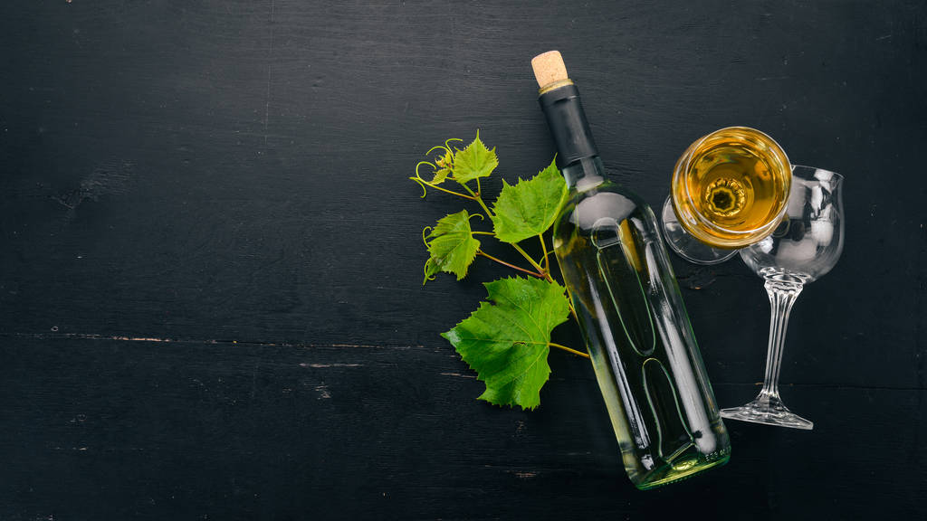 Uma garrafa de vinho branco com copos e uvas. Folhas de uvas. Vista superior. Em um fundo de madeira preto. Espaço livre para texto
. - Foto, Imagem