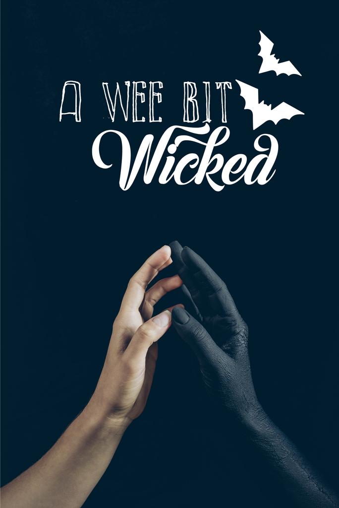 cropped view of woman touching with black demon hand isolated on black with "a wee bit wicked" lettering - Photo, Image