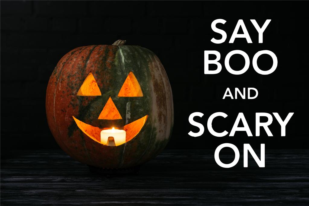 Jack o linterna de calabaza con vela en el interior de la mesa de madera sobre fondo negro con letras de halloween "say boo and scary on"
 - Foto, imagen