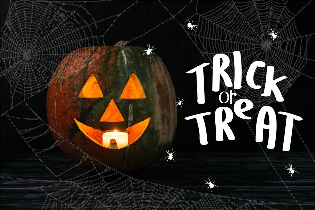 Jack o Laterne Kürbis mit Kerze drinnen auf Holztisch auf schwarzem Hintergrund mit "Trick or treat" Halloween-Schriftzug - Foto, Bild