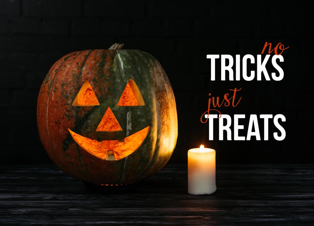 zucca spettrale halloween intagliato con candela su tavolo di legno su sfondo nero con scritta di Halloween "no tricks just Treats"
 - Foto, immagini