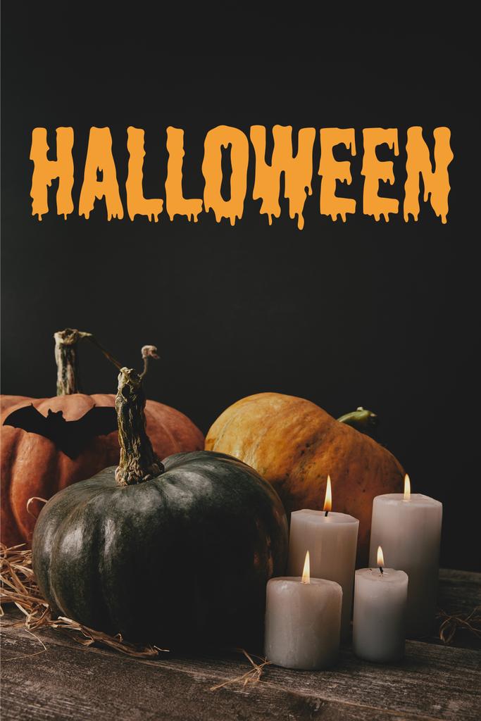 Kürbisse, schwarze Papierfledermaus und Kerzen auf dem Tisch mit "halloween" -Schriftzug - Foto, Bild