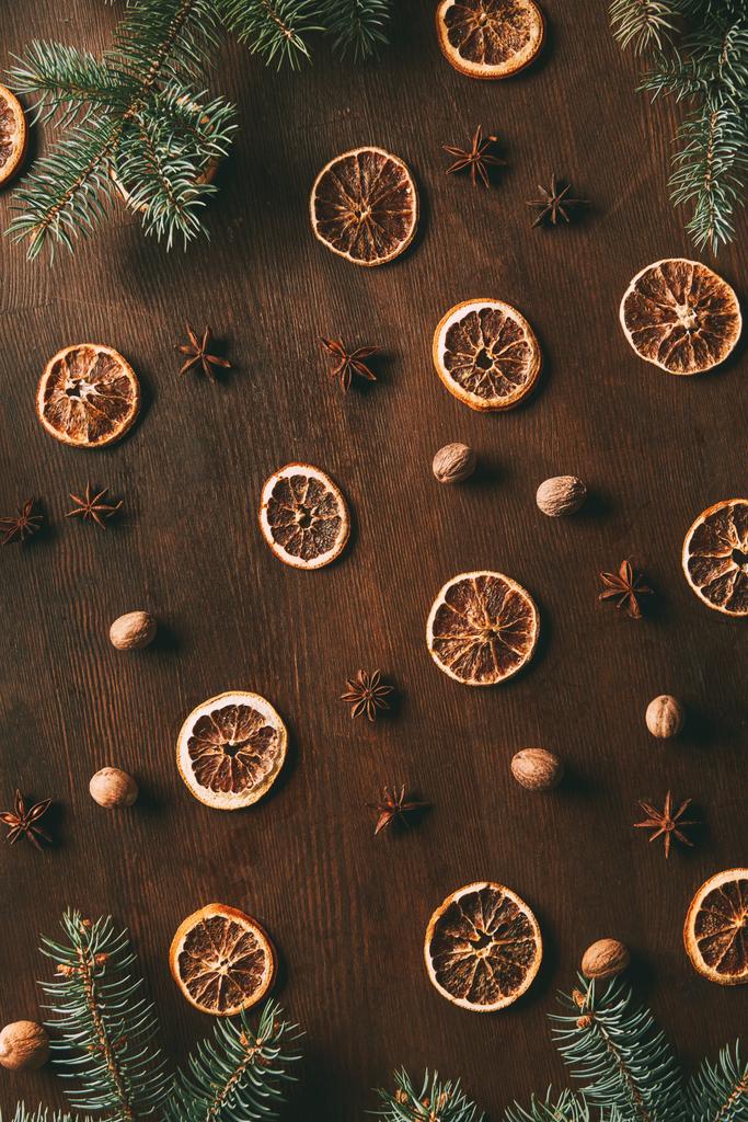 вид зверху на сушені апельсинові скибочки, зірки анісу та насіння мускатного горіха на дерев'яному фоні з ялиновими гілками
 - Фото, зображення