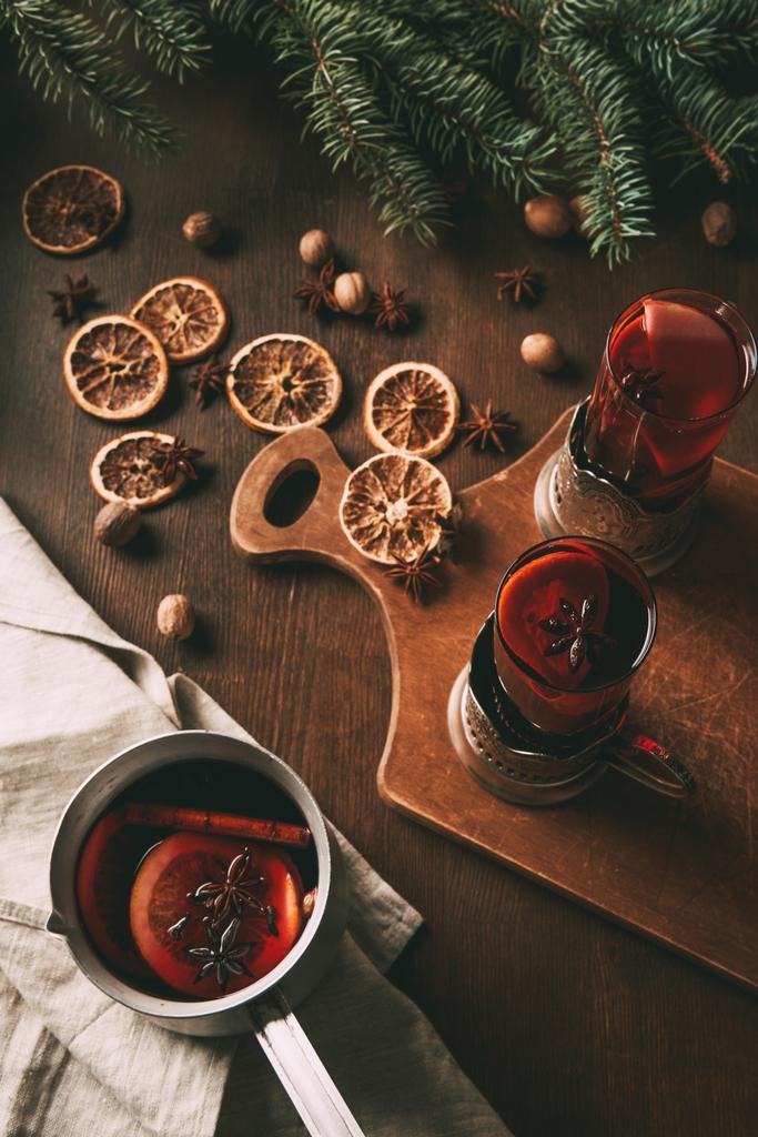 kuumaa glögiä kattilassa ja lasikuppeja leikkuulaudalla kuivattuja appelsiininviipaleita ja mausteita
  - Valokuva, kuva