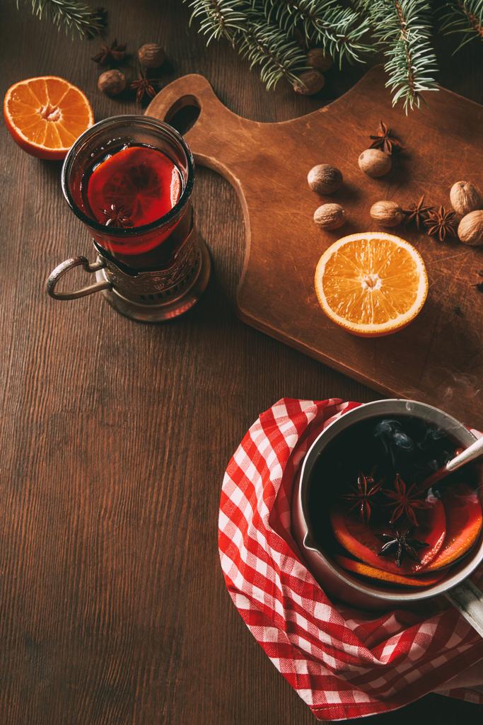 vin chaud chaud chaud maison dans une tasse en verre et une casserole avec des oranges fraîches et des épices sur fond en bois
  - Photo, image
