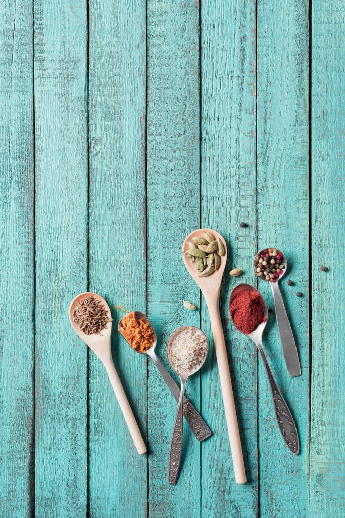 top view of spoons with various dried aromatic spices on turquoise wooden surface  - Photo, Image
