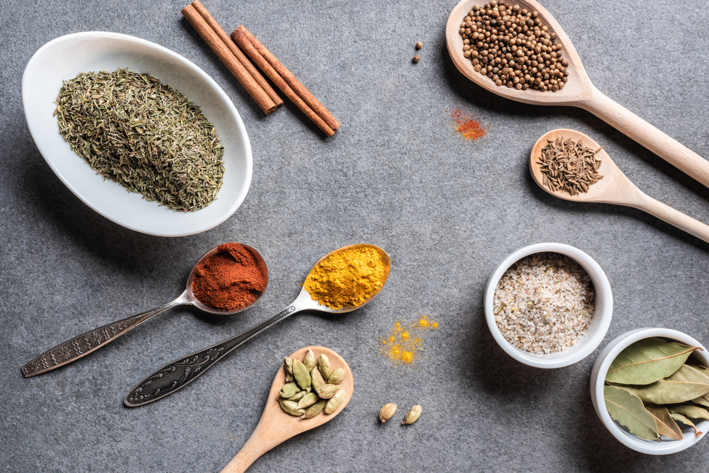 top view of various aromatic dried seasonings in bowls and spoons on grey surface    - Photo, Image