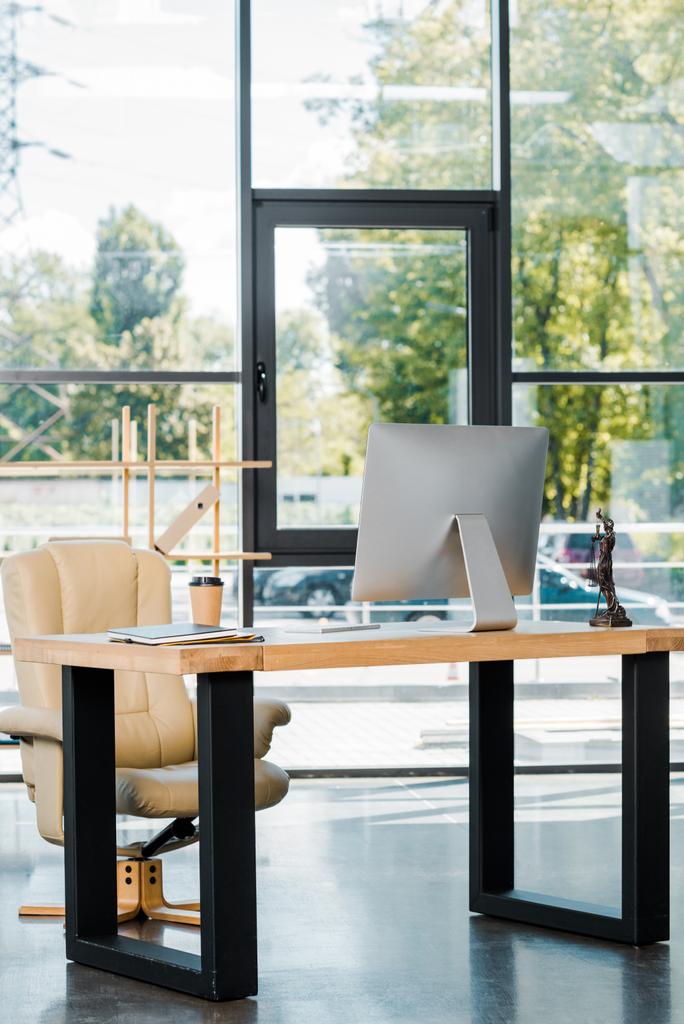 poltrona, mesa com computador, copo de café descartável e estátua themis no escritório de negócios
 - Foto, Imagem