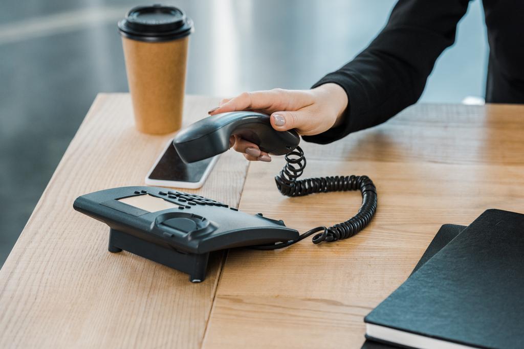 oříznutý obraz podnikatelka s sluchátko stacionární telefon v kanceláři - Fotografie, Obrázek