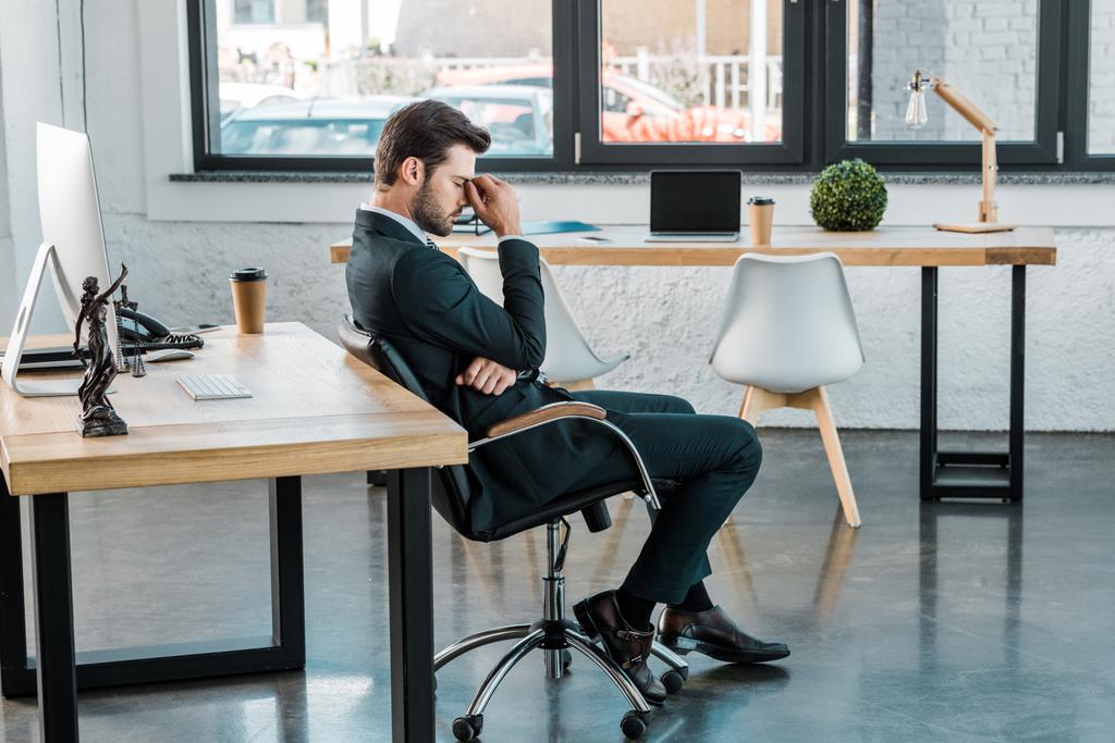 Seitenansicht eines müden Geschäftsmannes, der auf einem Stuhl sitzt und Nasenbrücke im Büro berührt - Foto, Bild