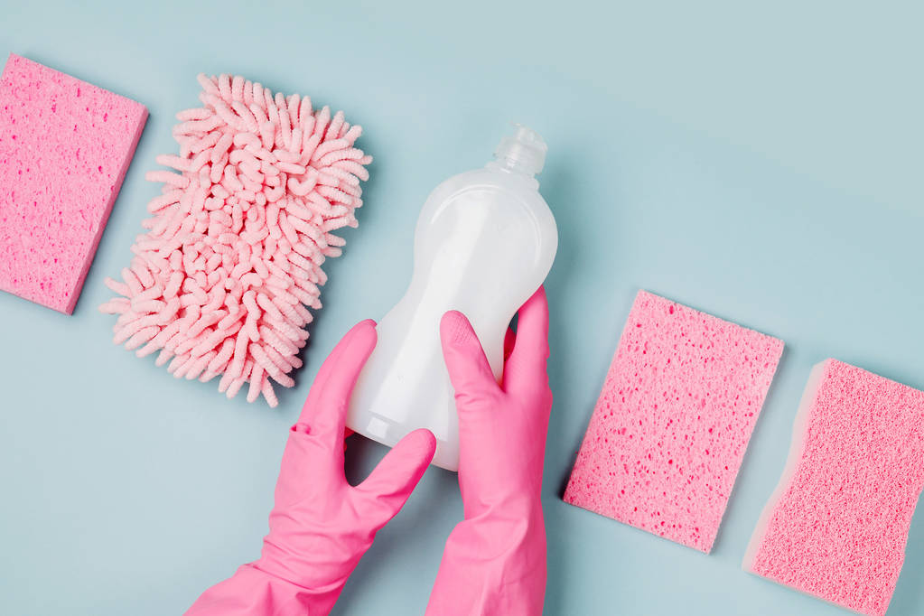 Hände in rosa Gummihandschuhen, die eine Flasche Reinigungsmittel mit Mikrofasertuch und Schwämmen halten - Foto, Bild