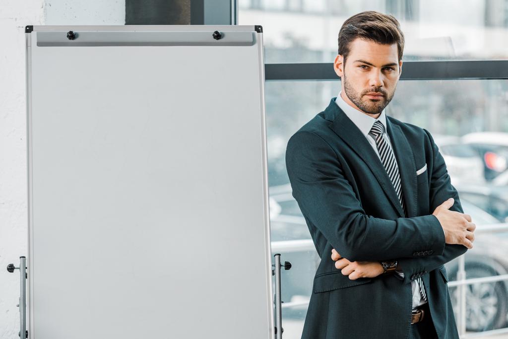 Portret van vertrouwen zakenman in pak staande op leeg wit bord in kantoor - Foto, afbeelding