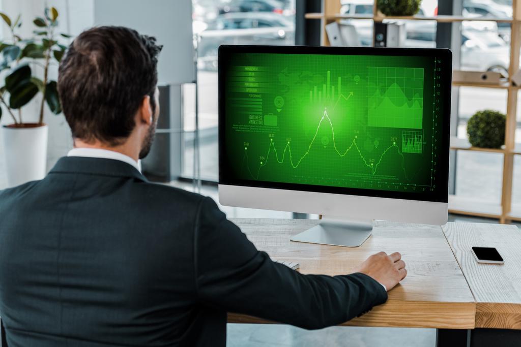 vista posterior del hombre de negocios en el lugar de trabajo con pantalla de computadora con diagrama en la oficina
 - Foto, imagen