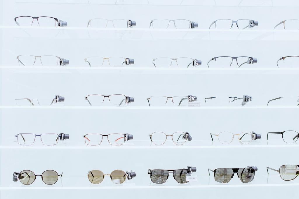estantes blancos con gafas de sol y anteojos elegantes en la tienda oftálmica
 - Foto, imagen